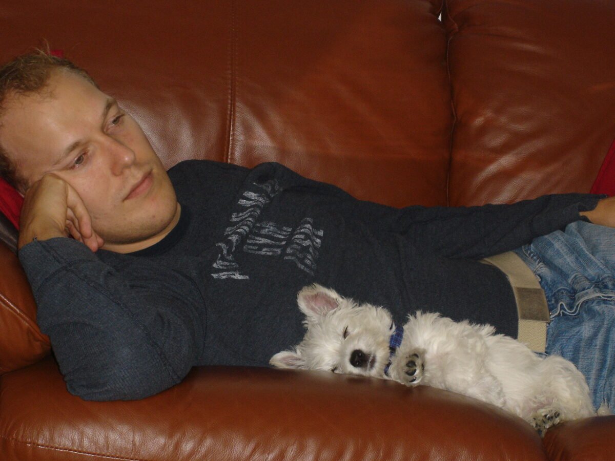 A man and his Westie puppy lying together on a sofa