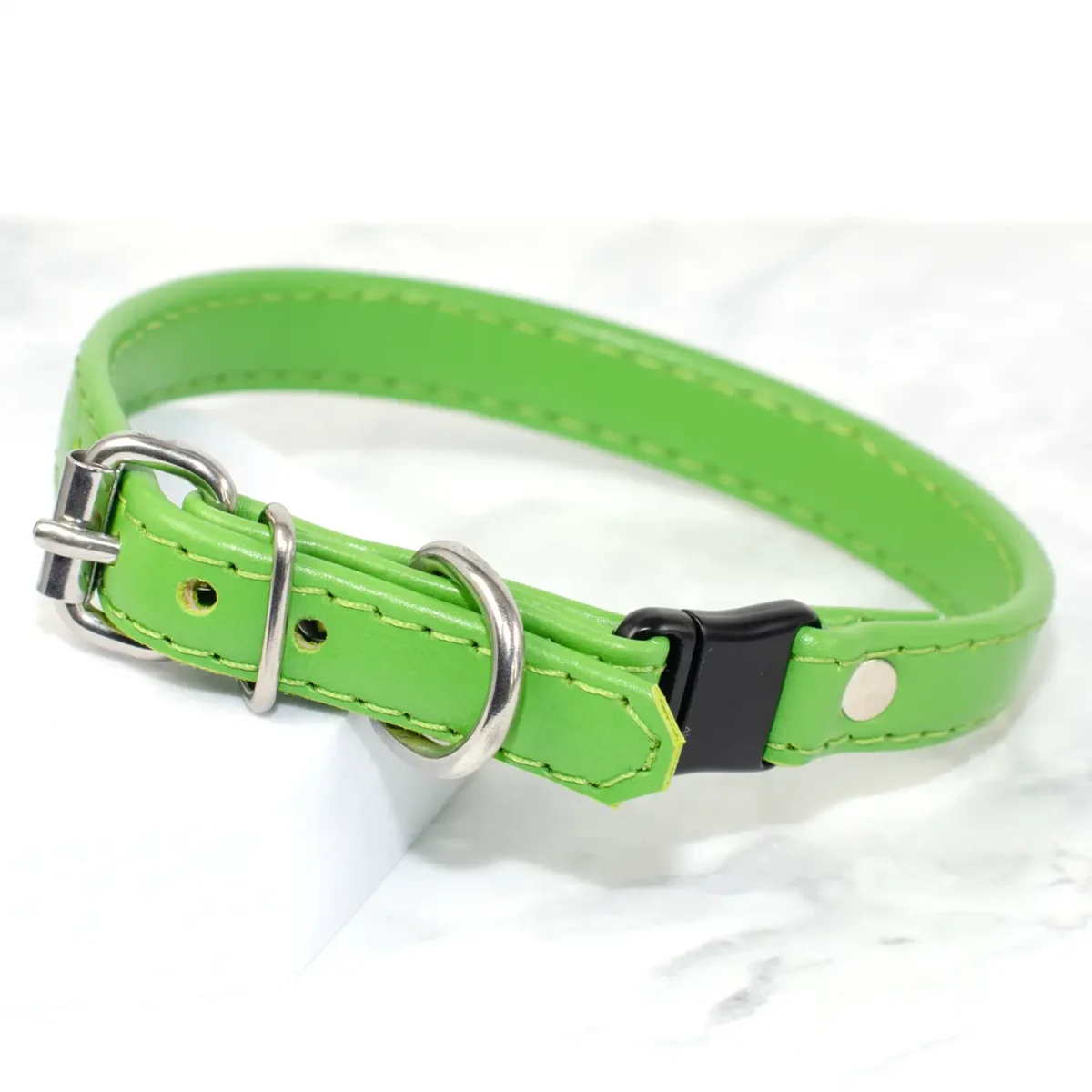 a bright, lime green, soft leather cat collar rests on a white marble background and is fitted with a safety buckle, handmade by Petiquette Collars