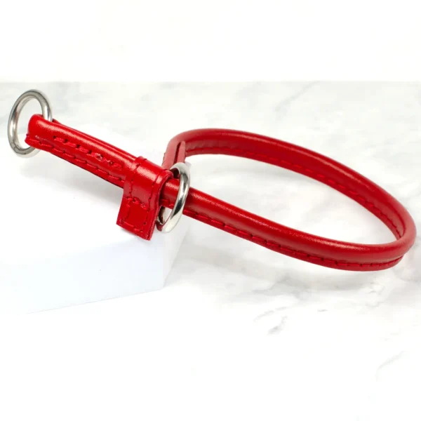a bright red leather slip collar for dogs with red leather keeper and stainless steel rings rests on white marble.
