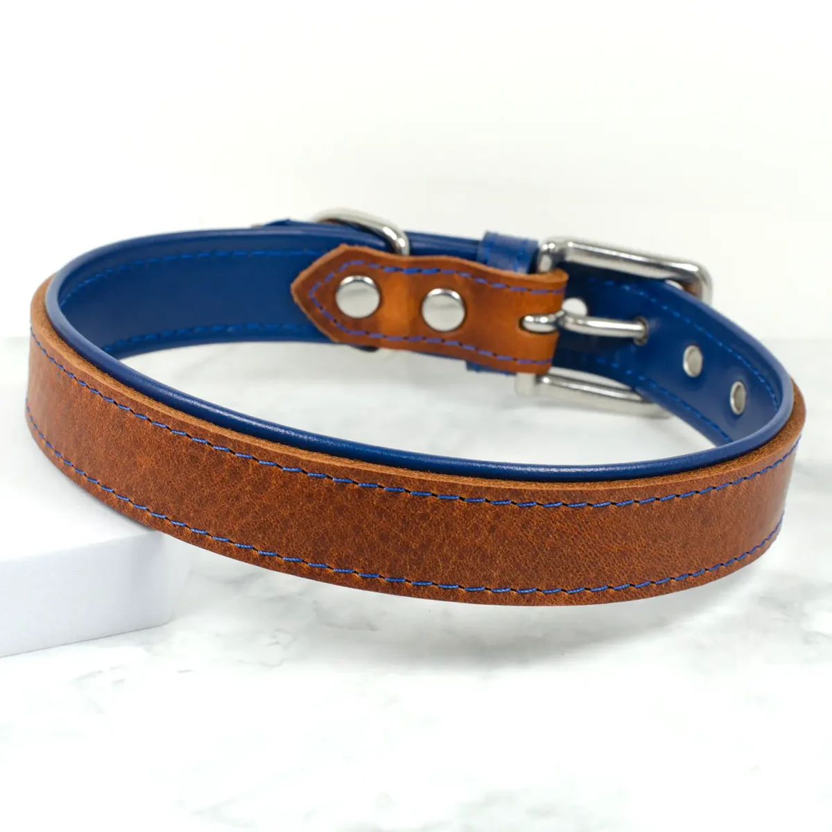 A brown and blue leather dog collar on a white marble background, handmade by Petiquette